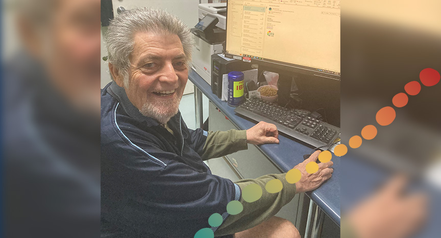 Man at desk, in front of computer, smiling