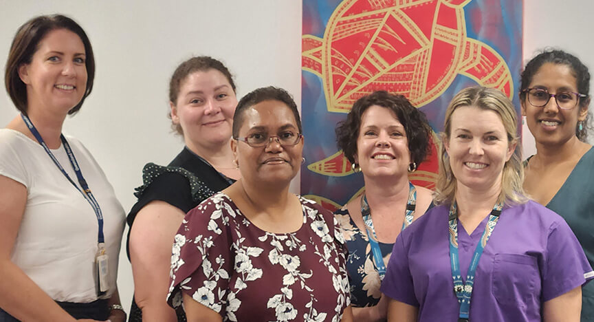 6 women smiling, standing in a group in front of artwork